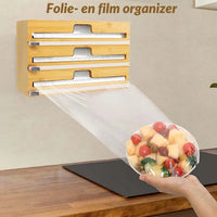 Wall-mounted bamboo 3-in-1 dispenser dispensing cling film over a bowl of fresh fruit held by hand in kitchen setting