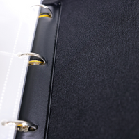 Close-up of black binder spine showing silver metal rings and yellow zipper teeth against textured dark fabric interior