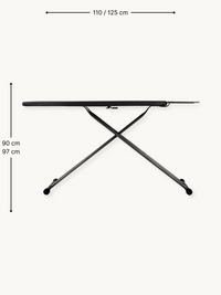 Black ironing board side view with cross steel frame, rubber feet, and iron rest, annotated with 110/125 cm width and 90/9…
