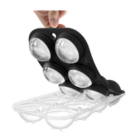Hand peeling black silicone top tray away from clear bottom tray, revealing six round ice spheres partially released from…