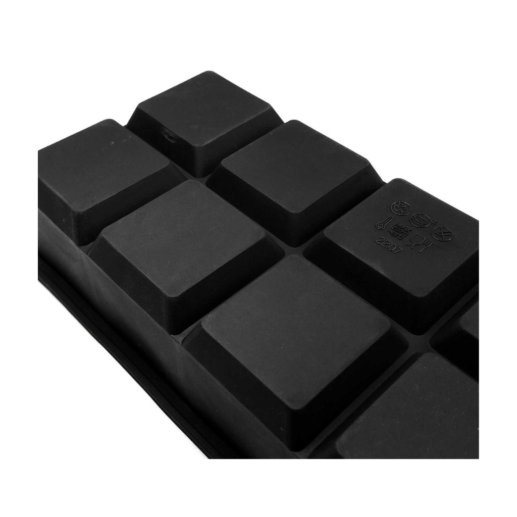 Close-up of black silicone square ice cube tray showing blank matte keycap-style cavities and moulded safety symbols on side