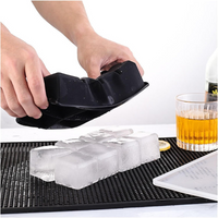 Hands peeling black silicone ice cube tray to release large clear ice cubes onto a bar mat, whisky glass alongside
