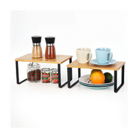 Two bamboo-top black metal cabinet risers styled with spice grinders, canned goods, mugs, plates, and fruit