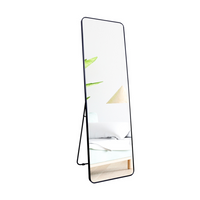 Black full-length floor mirror with rounded corners and thin brushed aluminium frame, shown freestanding with kickstand, a…