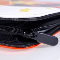 Close-up of black double zipper pull on orange-edged trading card binder, white printed top panel with gold star detail vi…