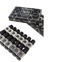 14 small fragrance oil bottles with black caps fanned out beside black geometric-patterned gift box, angled overhead view