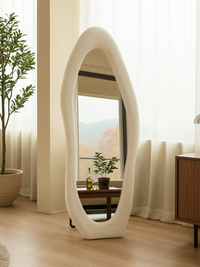 Seraphina full-length standing mirror with chunky asymmetric white teddy fabric frame, styled in bright living room beside…