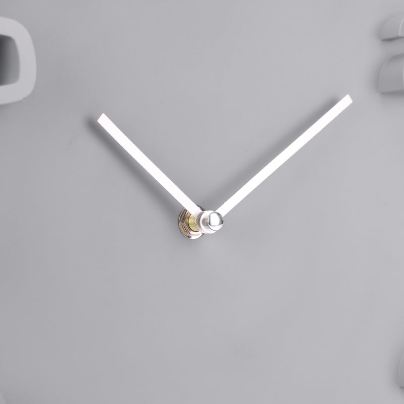 Close-up of white clock hands with silver centre fixing on grey clock face, partial raised numerals visible at edges