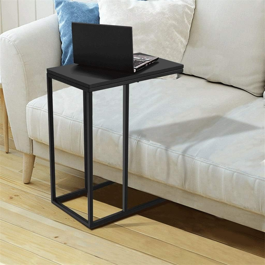 Black C-shaped side table beside a cream sofa, laptop resting on matte wood top, open steel base on light wood floor