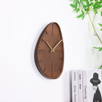 Dakar asymmetric brown resin wall clock mounted on white wall, angled side-profile lifestyle shot with books and plant nearby