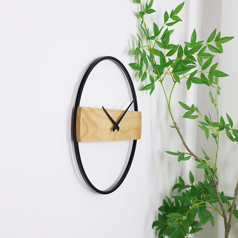 Reykjavik wall clock mounted on white wall at a slight angle, green plant branches visible alongside, showing black iron r…