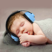 Sleeping newborn wearing blue and black ear defenders, hands tucked under chin, grey knit wrap, lifestyle close-up