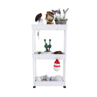 White 3-tier metal utility rack front view, styled with plants, a snowman ornament, and small toys across all three trays