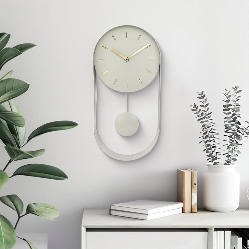 Pale green pendulum wall clock hung above a white sideboard with books and eucalyptus stems, green plant to the left, life…