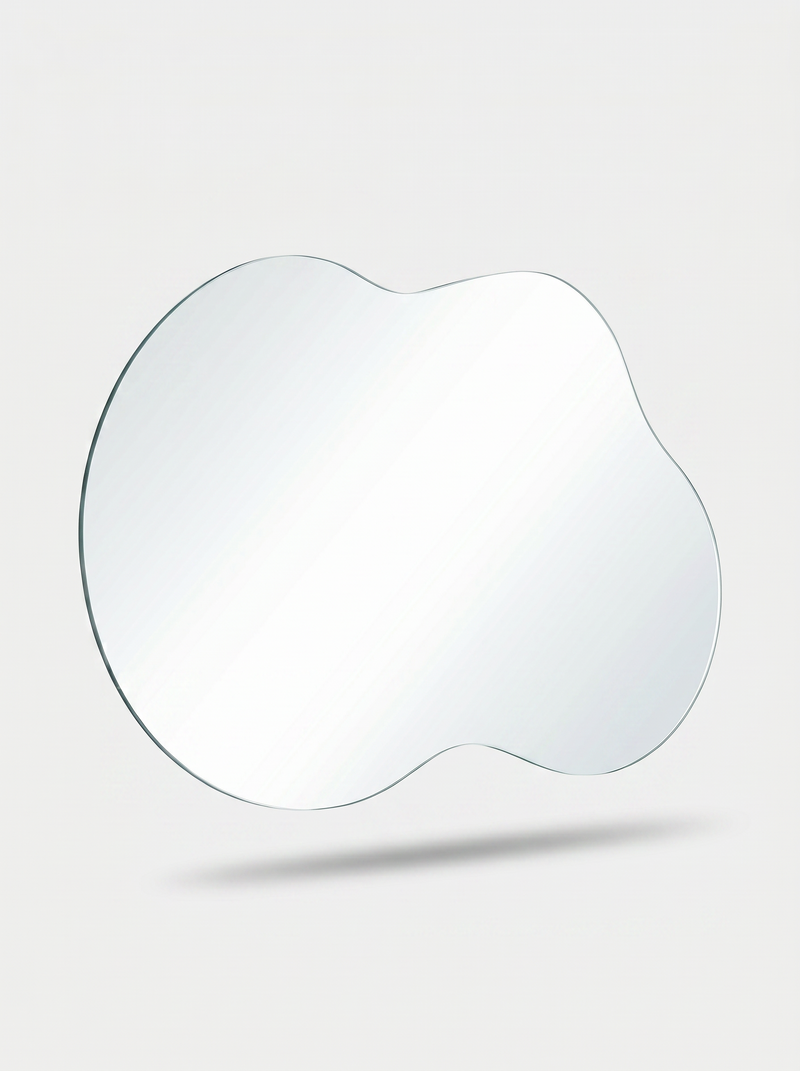 Frameless asymmetrical mirror with wavy cloud-like edge, angled three-quarter view showing slim tempered glass profile aga…