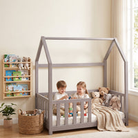 Two children playing with wooden blocks inside a clay gray house-shaped toddler bed with full safety rails, stuffed animal…