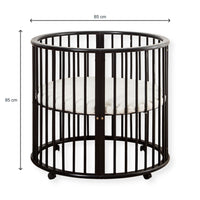 Black round wooden baby playpen with dimension annotations showing 85 cm width and 85 cm height, white mattress inside, on…