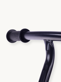 Close-up of black rubber handlebar grip end on dark steel handlebar, showing textured perforated pattern and stem weld joint