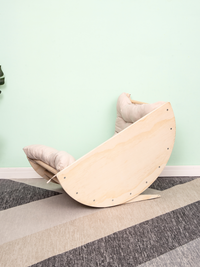 Side view of birch climbing arch tipped at an angle showing smooth underside and screw details, cream cushion visible behi…
