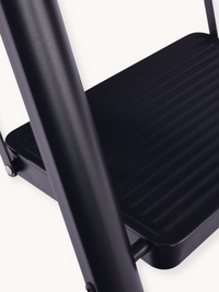 Close-up of black metal step ladder showing ribbed anti-slip tread surface and tubular frame junction detail