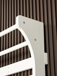 Close-up of white climbing frame top corner panel showing two silver screws and curved arch detail against dark slatted wall