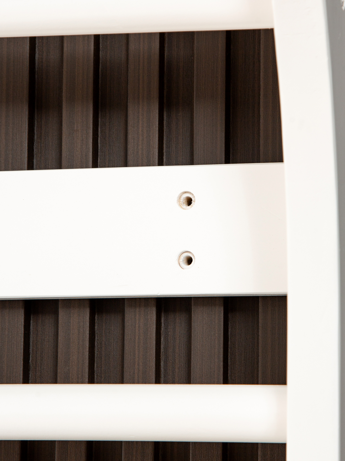 Close-up of white frame rail showing two pre-drilled screw holes against dark wood slatted wall panels