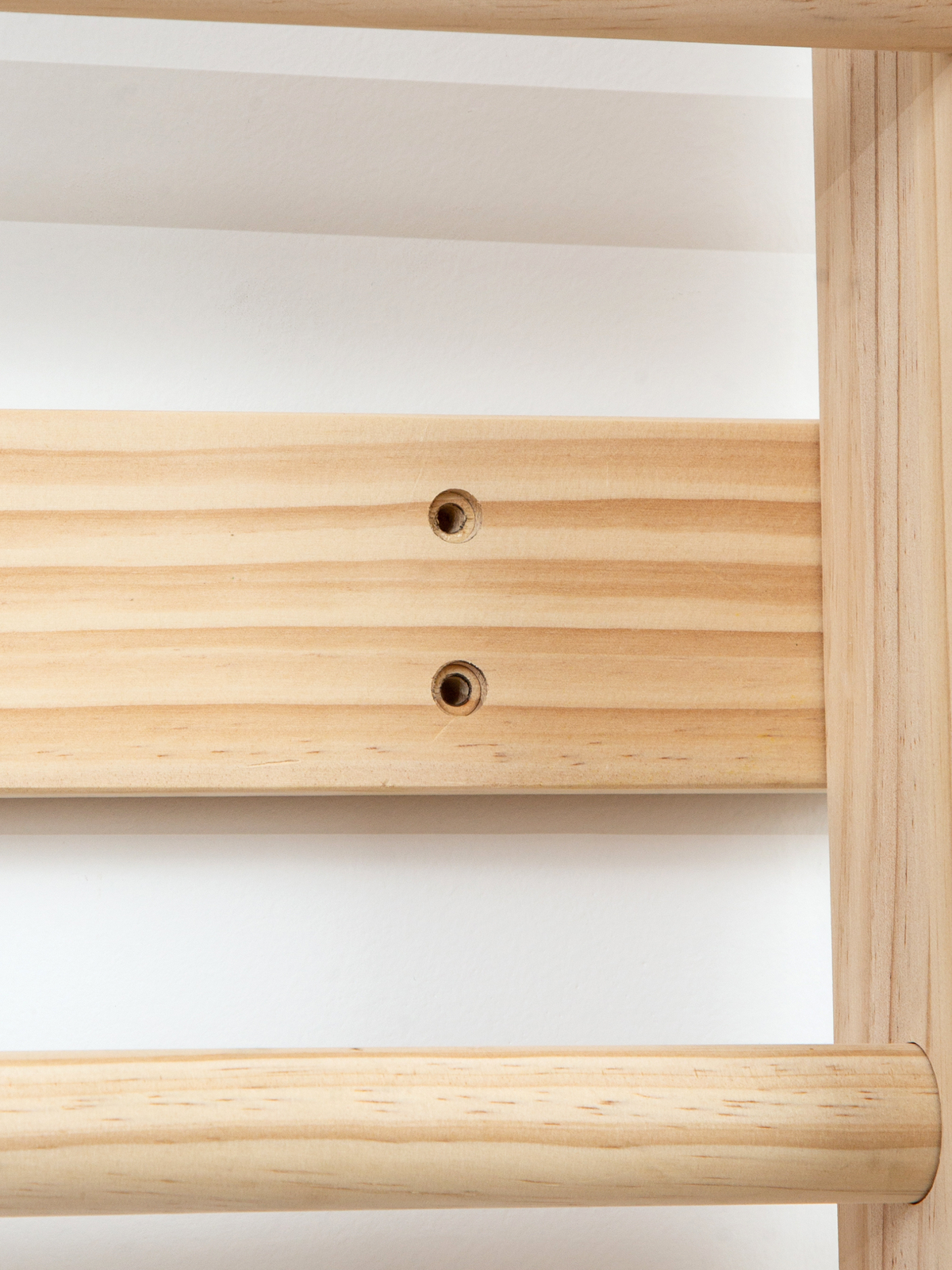 Close-up of natural wood climbing frame showing two pre-drilled screw holes on a flat side rail beside a rounded rung and…