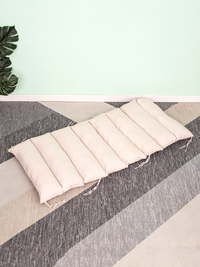 Cream segmented floor cushion with tie strings laid flat on grey striped carpet, monstera plant and mint wall in background