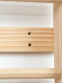 Close-up of natural pine wood panel showing two pre-drilled screw holes, with rounded dowel rung and frame rail visible