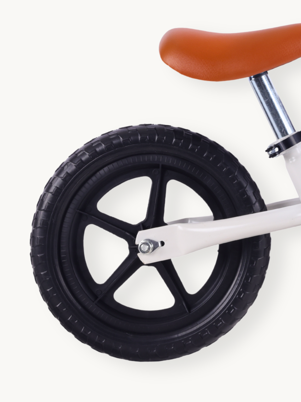 Close-up of rear wheel on white balance bike, showing black rubber knobbed tire, five-spoke plastic rim, and tan saddle above