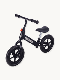 Black New Speed balance bike angled side view, steel frame with orange seat clamp bolt, rubber grip tires and padded saddle