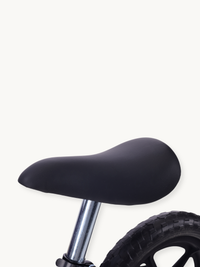 Close-up of black padded saddle on chrome steel seatpost, with partial five-spoke black rim and knobby rubber tire visible