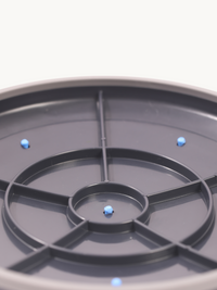 Dark grey balance disc bottom view showing central spoke frame and three blue anti-slip studs on white background