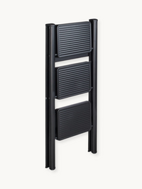 Black 3-step folding ladder collapsed flat, front angle view showing three ribbed dark grey steps between slim black metal…