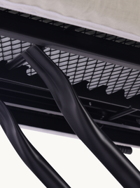 Close-up of black steel mesh shelf and curved cross-frame legs underneath a taupe ironing board, showing underside constru…