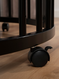 Close-up of black locking castor wheel on black round wooden playpen base, light oak floor below