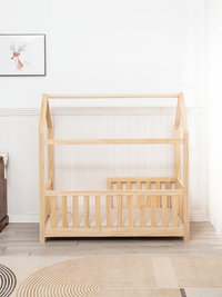 Natural pine toddler house bed with triangular roof frame and spindle safety rails, front view in bright nursery, no mattr…