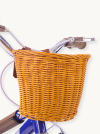 Golden-tan wicker front basket with brown leather straps attached to chrome handlebars of a dark blue children's bike