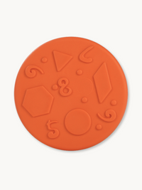 Orange balance disc flat lay showing embossed shapes and numbers including triangle, hexagon, circle, and diamond on textu…