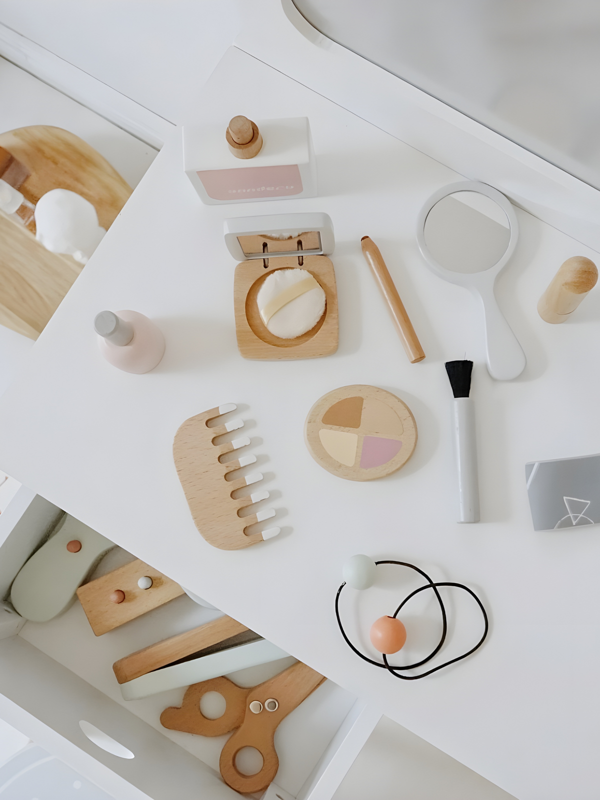 Overhead flatlay of wooden toy beauty accessories including comb, compact, eyeshadow palette, brush, mirror, and scissors…