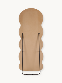 Rear view of wavy full-length mirror flat on surface, taupe beige suede velvet back and black metal folding easel stand vi…