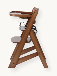 Side profile of walnut wood high chair showing A-frame legs, adjustable footrest, black safety harness, and attached tray…