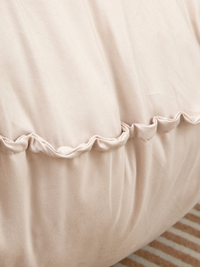 Close-up of ruched scalloped seam running across the middle of a cream white floor cushion, soft fabric folds visible abov…