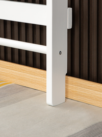 Close-up of white climbing frame leg base resting on grey carpet against natural oak skirting board and dark slatted wall