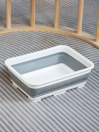 Grey and white collapsible square storage bin shown removed from climbing arch, placed on grey striped rug with wooden fra…