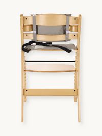 Natural wood highchair front view with grey padded cushion, black safety harness, and lower footrest shelf visible