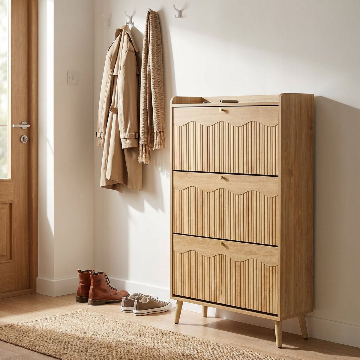 Light oak three-tier shoe cabinet with ribbed flip-down doors styled in a hallway with coats, boots, and sneakers nearby