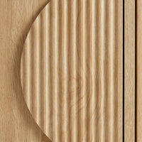 Close-up of circular ribbed door detail on light oak TV stand, showing vertical grain texture contrast against flat panel