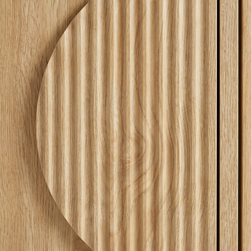 Close-up of circular ribbed door detail on light oak TV stand, showing vertical grain texture contrast against flat panel