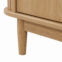Close-up of tapered oak leg and rounded base rail corner on light oak TV stand, showing natural wood grain detail